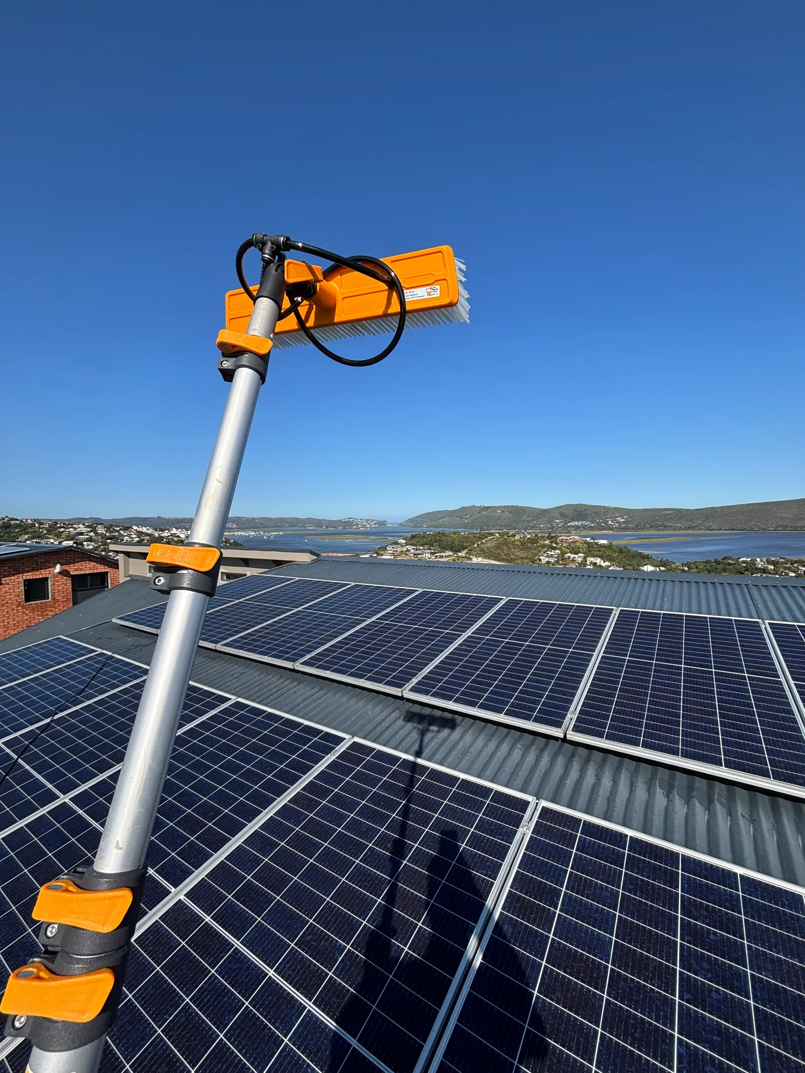 Solar-panel cleaning brush above rooftop panels overlooking Knysna lagoon